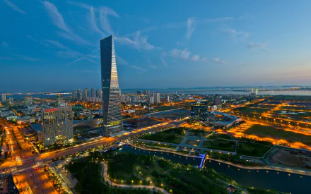 HD PC desktop wallpaper showcasing the modern man-made skyline of Incheon at dusk, highlighting illuminated buildings and a prominent skyscraper against a blue sky.