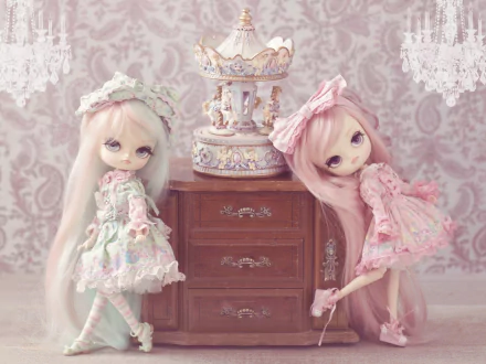 A charming HD wallpaper featuring two man-made dolls in pastel outfits, posing beside an ornate music box on a vintage dresser against a delicate patterned background.