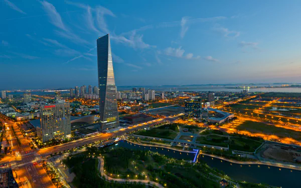 HD PC desktop wallpaper showcasing the modern man-made skyline of Incheon at dusk, highlighting illuminated buildings and a prominent skyscraper against a blue sky.