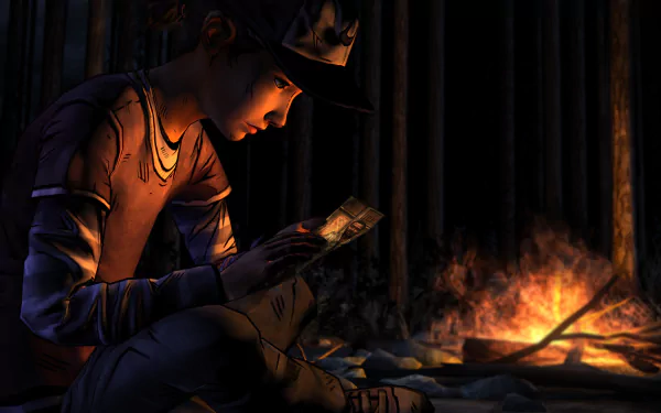 HD PC desktop wallpaper from The Walking Dead: Season 2 video game, showing a character sitting by a campfire examining a small object in a dark, wooded setting.