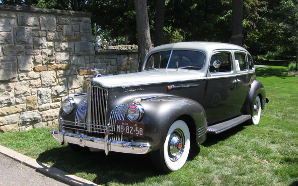 HD PC desktop wallpaper background: polished gray Packard 180 vehicle — vintage sedan with chrome grille and whitewall tires parked on a lawn beside a stone wall.