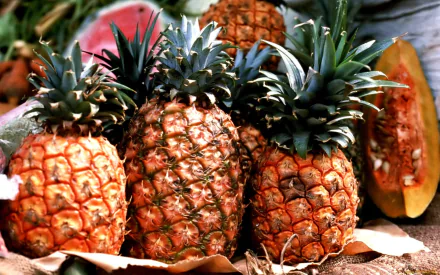 HD PC desktop wallpaper featuring a vibrant close-up of fresh pineapples, highlighting their textured skin and green leafy tops among other tropical fruits.