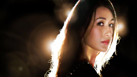 HD desktop wallpaper of Maggie Q from the TV show Nikita, featuring a dramatic, well-lit portrait with a dark backdrop and lens flare effects.