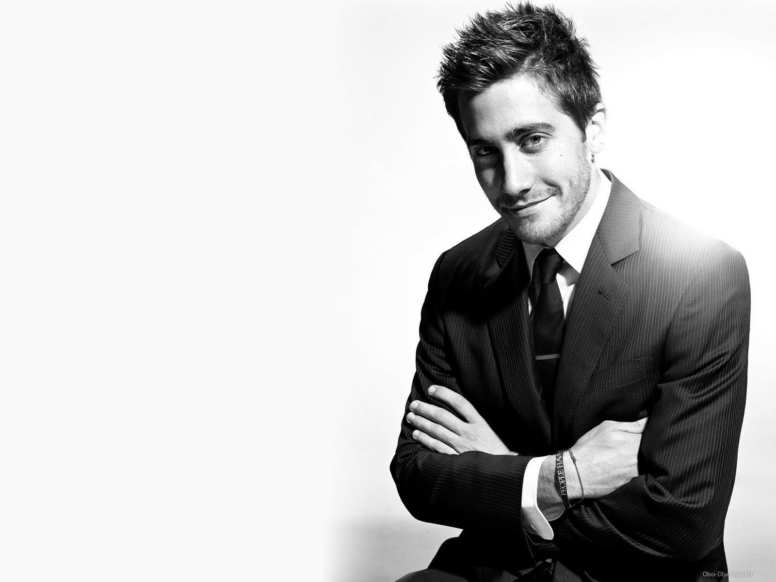 Black and white HD desktop wallpaper of celebrity Jake Gyllenhaal in a suit, smiling with arms crossed against a light background.
