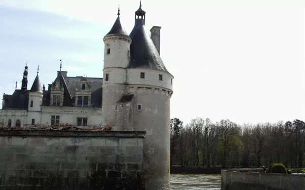 HD desktop wallpaper featuring the man-made Château de Chenonceau with its distinctive towers overlooking a river against a cloudy sky backdrop.
