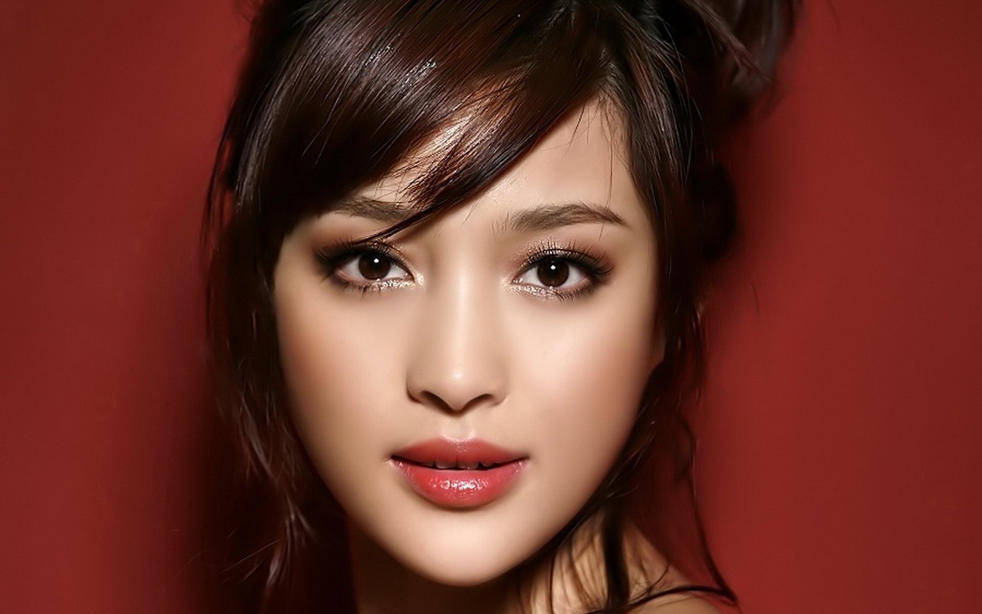 HD desktop wallpaper featuring a close-up portrait of a Korean woman with flawless makeup and styled hair against a deep red background.