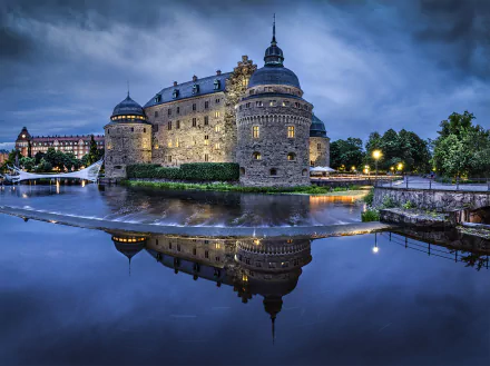 HD wallpaper featuring Orebro Castle in Sweden at night, illuminated and perfectly reflected in the calm water below.