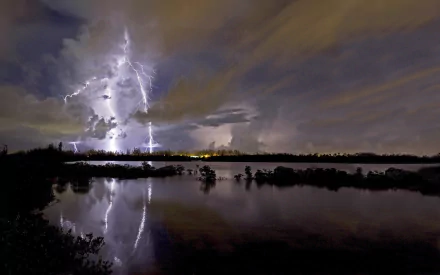 A stunning HD wallpaper featuring dramatic lightning striking through dark clouds, reflecting on a calm body of water, capturing the raw power of nature in a striking landscape.