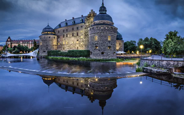 HD wallpaper featuring Orebro Castle in Sweden at night, illuminated and perfectly reflected in the calm water below.