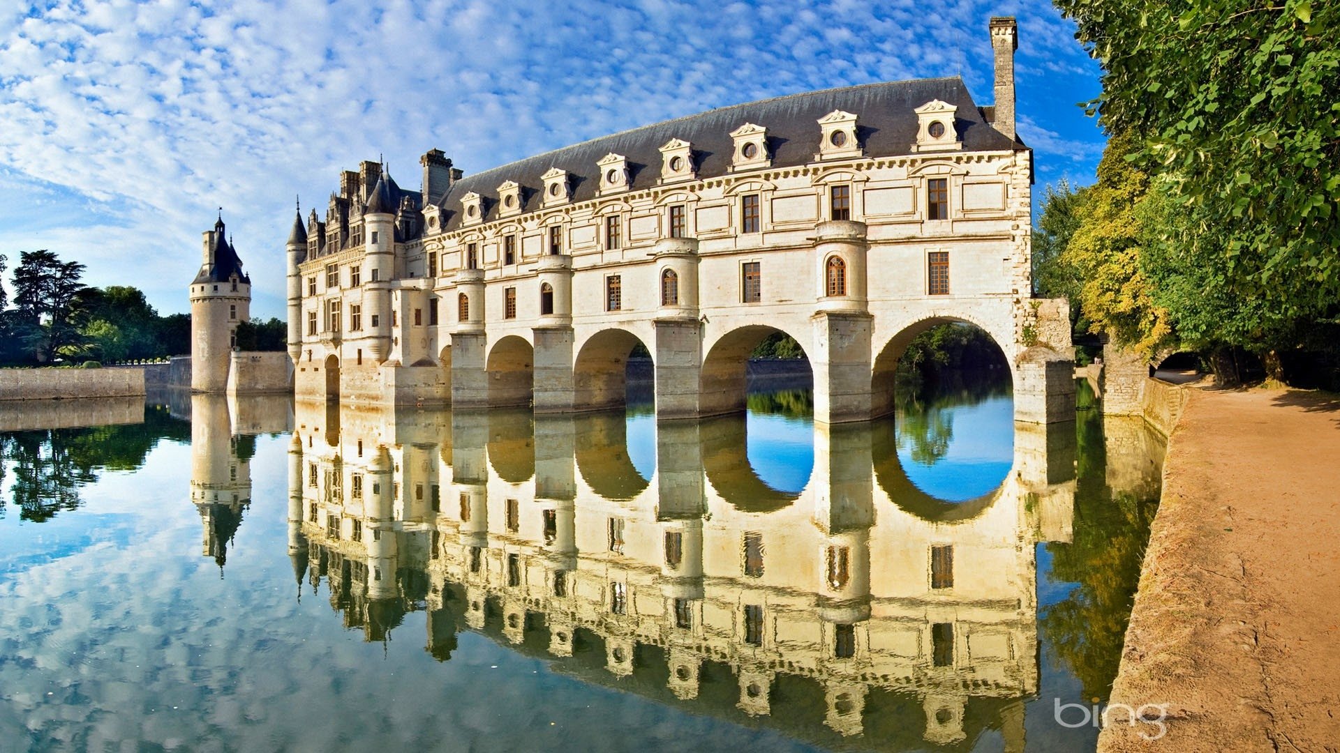 A stunning view of Château de Chenonceau in France, showcasing its elegant architecture and reflection in the calm waters, surrounded by lush greenery.