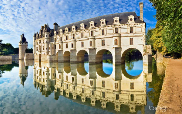 A stunning view of Château de Chenonceau in France, showcasing its elegant architecture and reflection in the calm waters, surrounded by lush greenery.