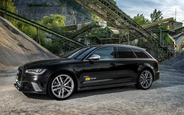 HD PC desktop wallpaper of a black Audi RS6 Avant vehicle parked in a gravel quarry with rusted conveyors and a dramatic sky.