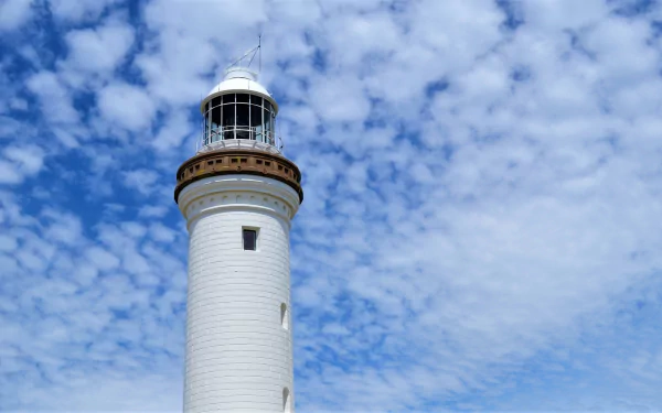 Close-up of Norah Head Lighthouse in Australia against a partly cloudy blue sky, featured as an HD PC desktop wallpaper and background.