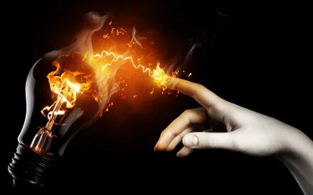 A dramatic image of a hand reaching toward a glowing light bulb, with sparks and flames, showcasing creativity and energy. This HD desktop wallpaper features striking contrasts and vivid colors.