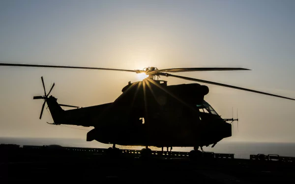 Silhouetted military Aérospatiale SA 330 Puma helicopter on a ship deck at sunset, sunburst through the rotors — 4K Ultra HD PC desktop wallpaper and background.