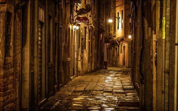 A dimly lit Venetian alley at night, featuring cobblestone streets and charming buildings, captures the essence of Italy's enchanting atmosphere in this HD desktop wallpaper.
