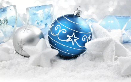 A festive arrangement of blue and silver Christmas ornaments surrounded by soft snow and decorative stars, creating a joyful holiday scene for a vibrant desktop wallpaper.