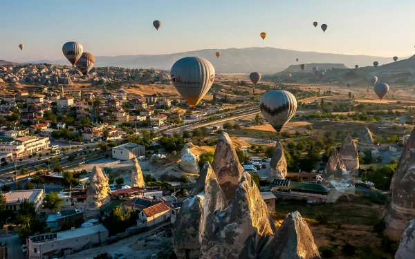 HD desktop wallpaper featuring numerous hot air balloons floating over a rocky landscape and town during sunrise or sunset.