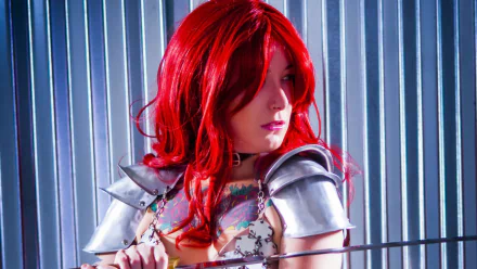 HD PC desktop wallpaper featuring a woman cosplaying as Red Sonja, with vibrant red hair and detailed armor against a metallic striped background.