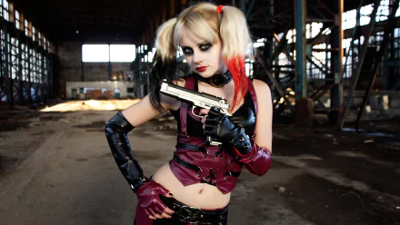 A woman in Harley Quinn cosplay holds a gun confidently, showcasing vibrant red and black attire in an industrial setting. This striking image serves as a dynamic HD desktop wallpaper.