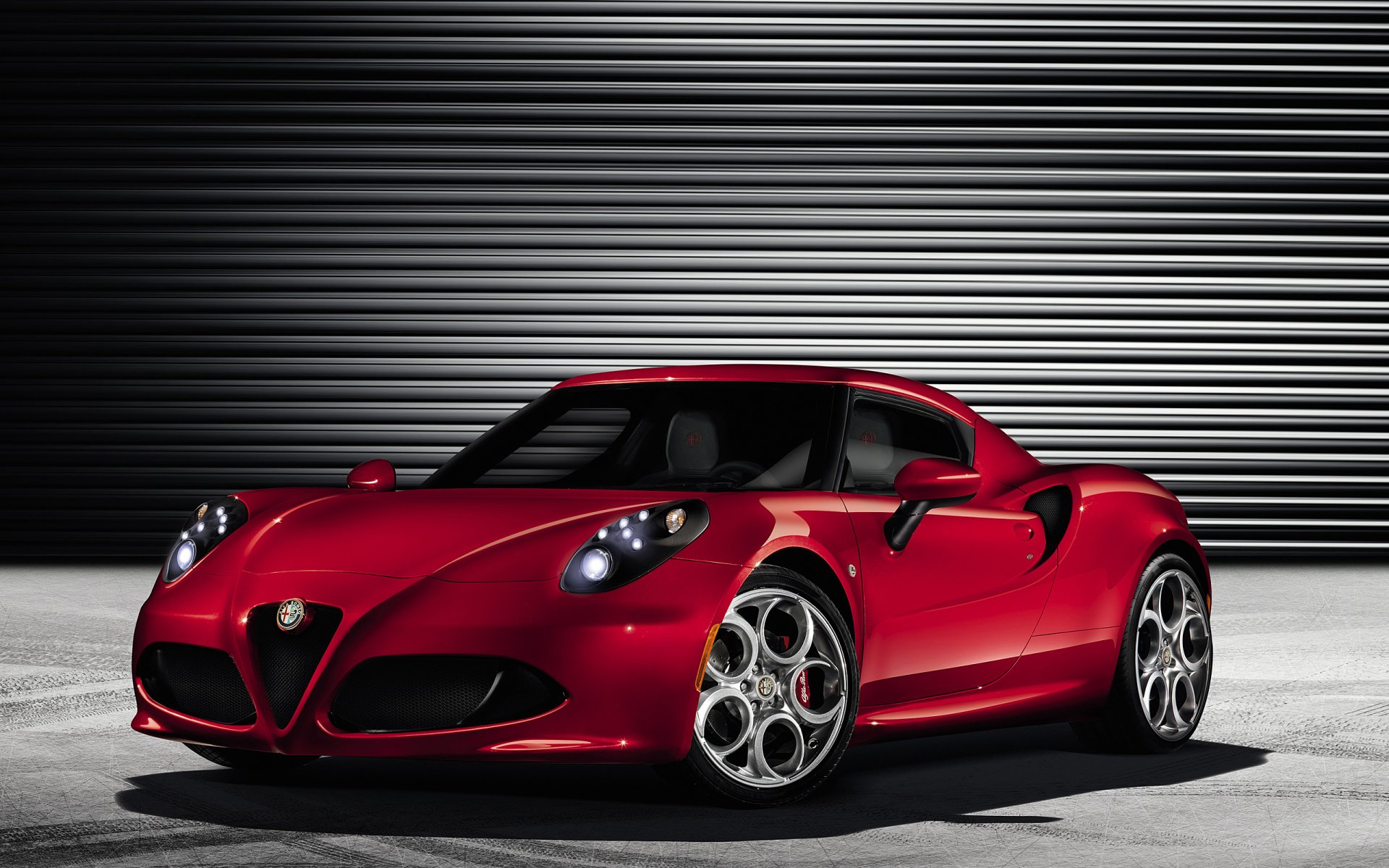 Red Alfa Romeo 4C vehicle parked against a ribbed metal backdrop, high‑detail 2K Quad HD PC desktop wallpaper.