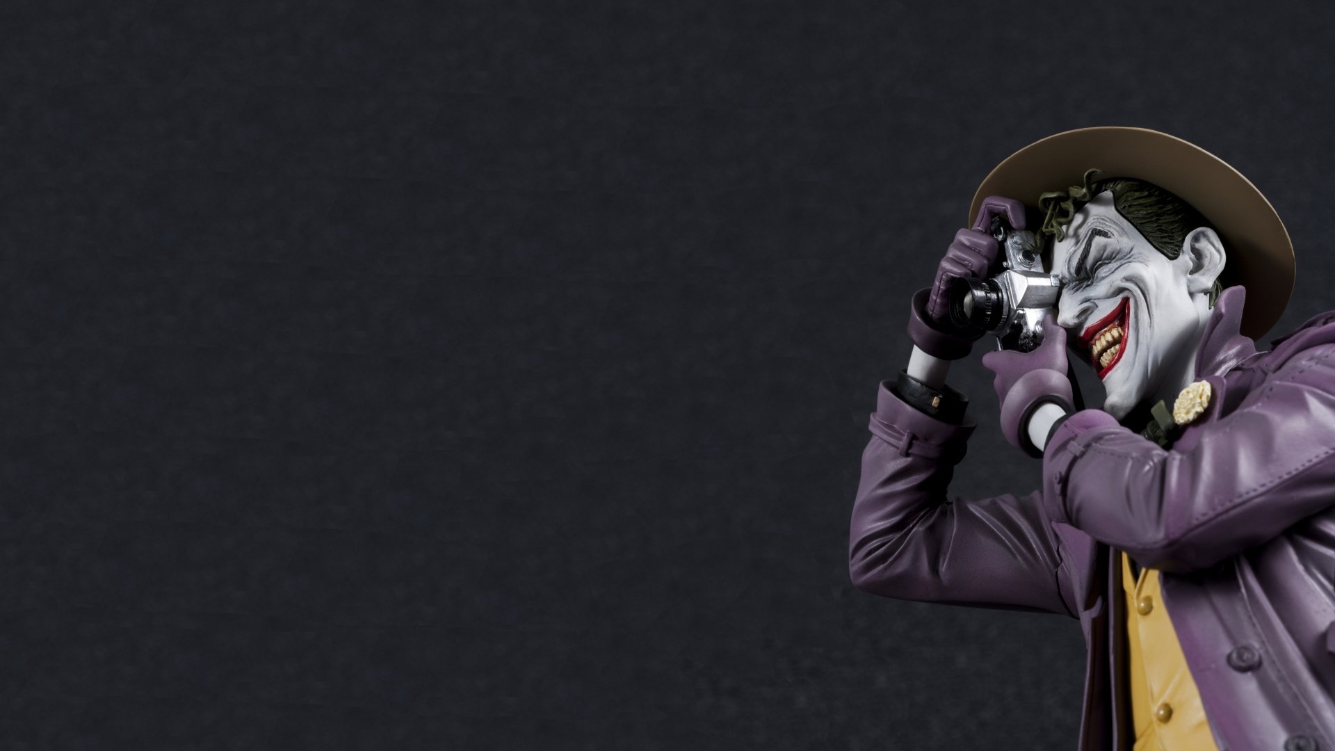 A vibrant HD wallpaper featuring the Joker from *Batman: The Killing Joke*, capturing his iconic pose with a camera against a dark background.