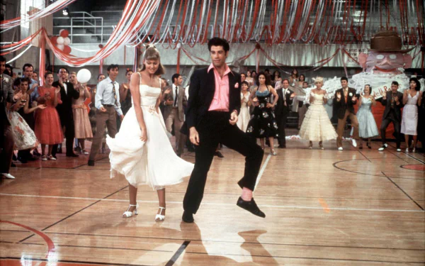 HD PC desktop wallpaper featuring a vibrant dance scene from the movie Grease, showcasing iconic characters at a high school gym decorated for a dance.