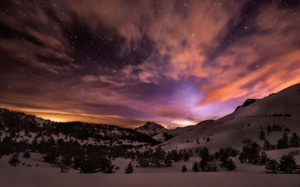 HD PC desktop wallpaper showing a dramatic night sky with stars and clouds over a snowy mountain landscape in nature.