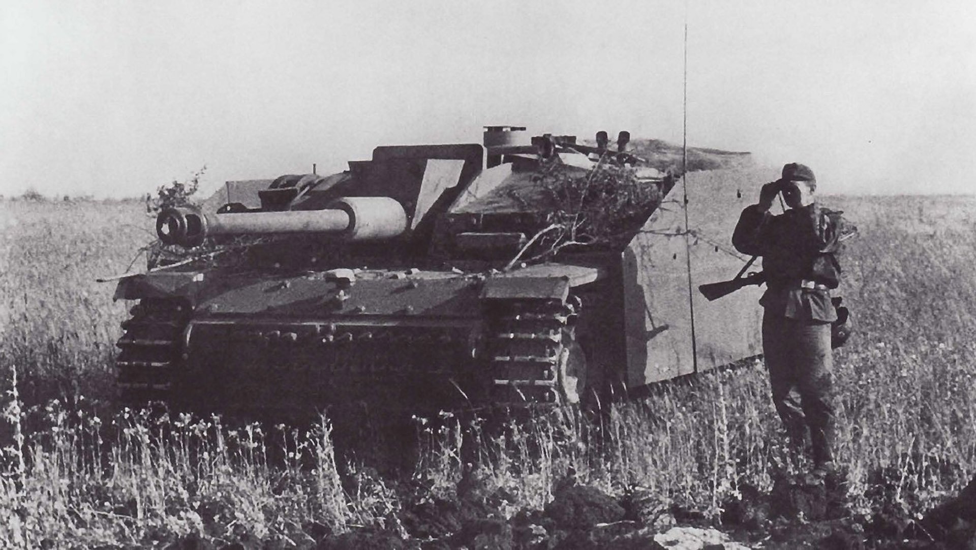 Black-and-white HD military desktop wallpaper showing a tank in a field with a soldier standing beside it, capturing a wartime scene.