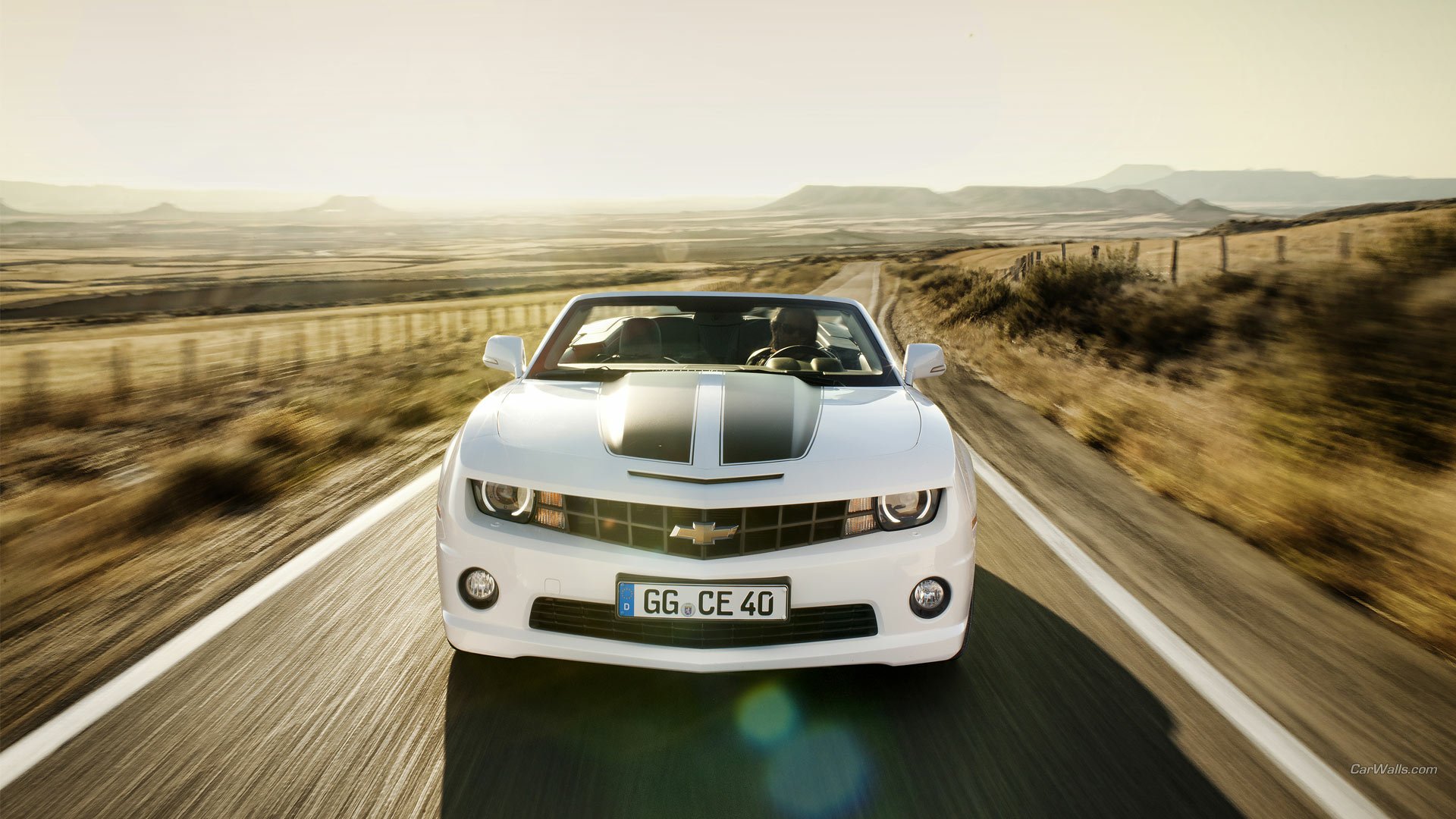 A white Chevrolet Camaro Convertible drives on an open road through a sunlit desert landscape, captured in a high-definition PC desktop wallpaper.