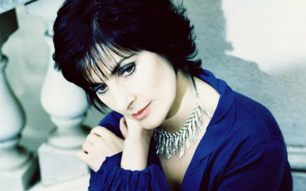 HD PC desktop wallpaper: portrait of a contemplative female singer in a blue top wearing a silver fringe necklace, music-themed background.