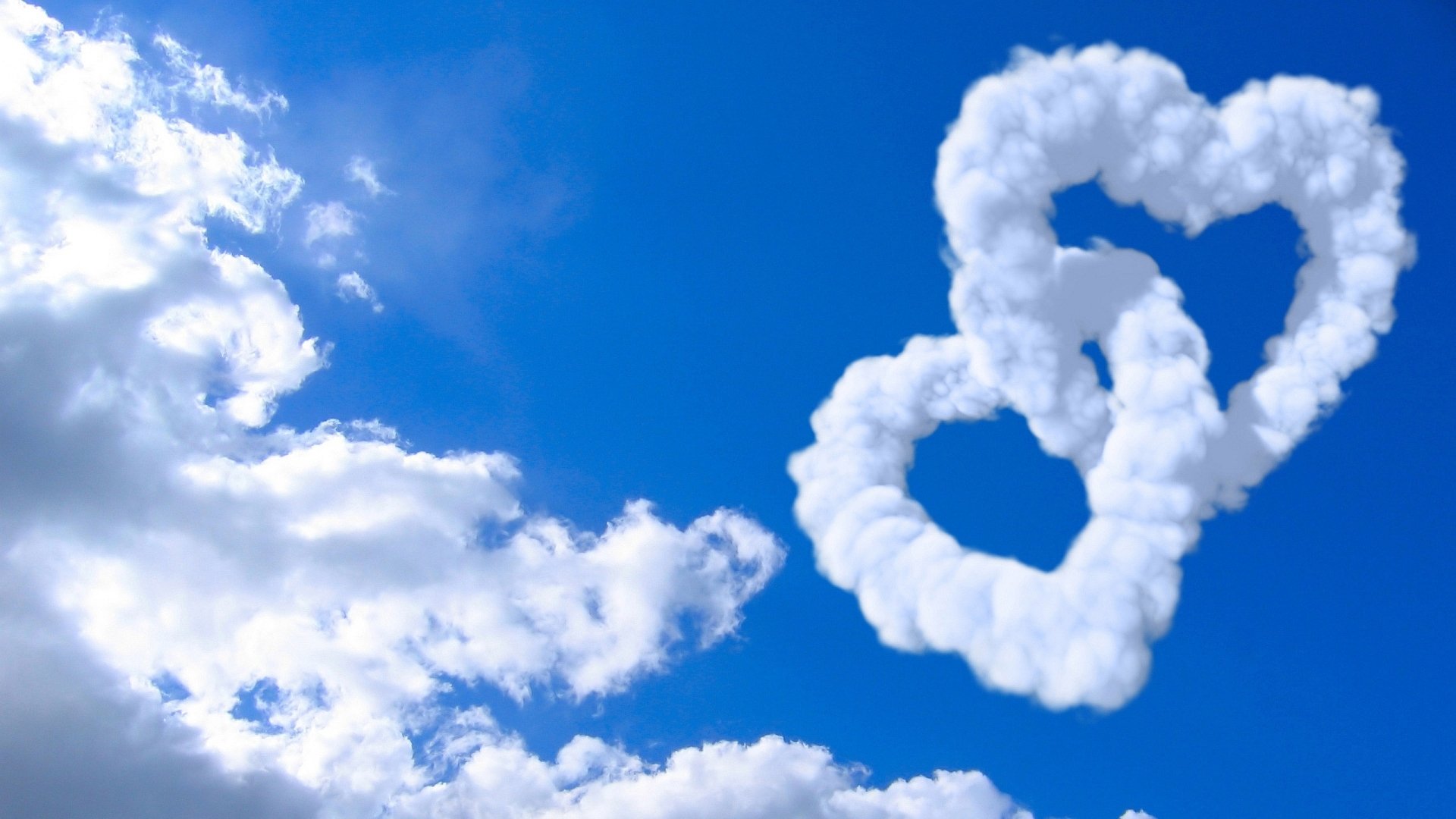Artistic HD desktop wallpaper featuring a bright blue sky with clouds shaped like two intertwined hearts.