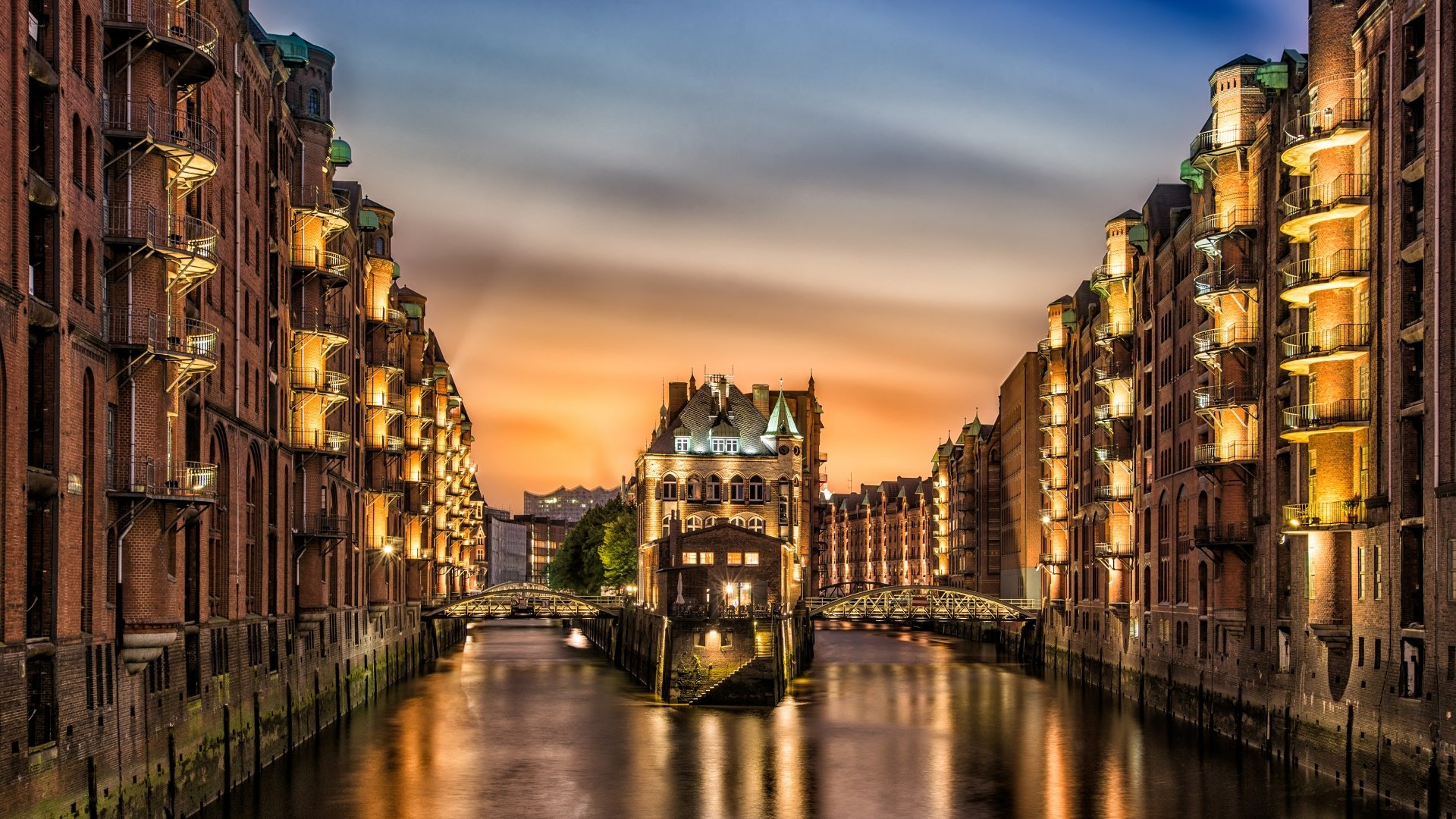 A stunning HD wallpaper of Hamburg, Germany, showcasing picturesque man-made architecture along a tranquil canal at sunset, illuminated by warm lights.