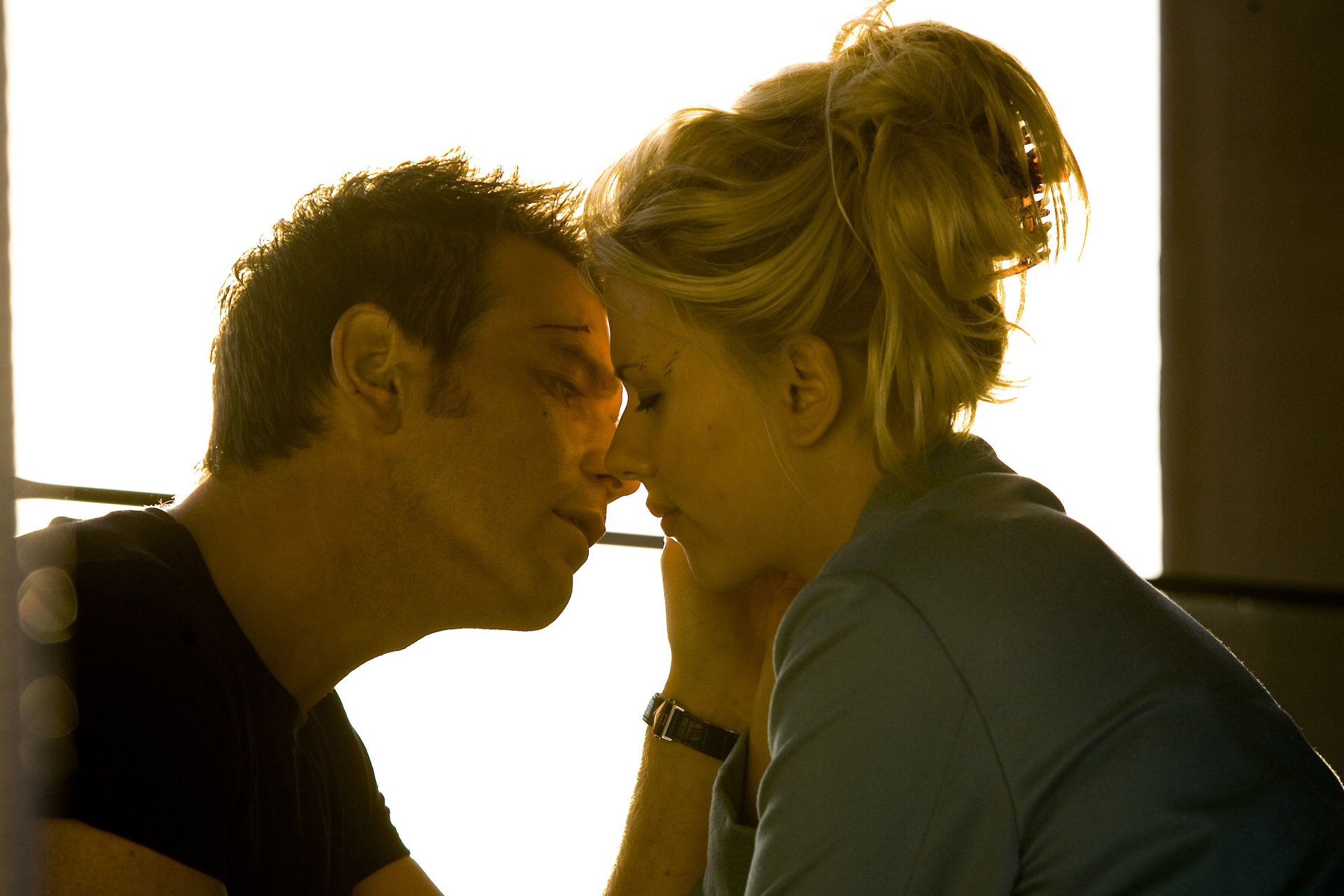 Film still from The Island: two actors in an intimate, backlit close-up with faces inches apart, warm tones — 2K Quad HD PC desktop wallpaper.