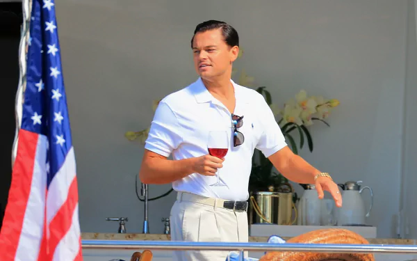HD wallpaper of Leonardo DiCaprio as Jordan Belfort in 'The Wolf of Wall Street,' with an American flag in the background.