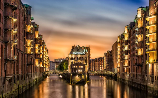 A stunning HD wallpaper of Hamburg, Germany, showcasing picturesque man-made architecture along a tranquil canal at sunset, illuminated by warm lights.