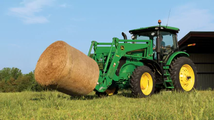A green John Deere tractor lifting a large round hay bale in a grassy field, captured in 4K Ultra HD for a PC desktop wallpaper.