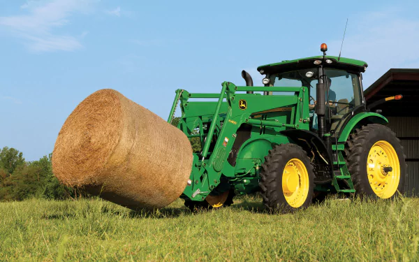 A green John Deere tractor lifting a large round hay bale in a grassy field, captured in 4K Ultra HD for a PC desktop wallpaper.