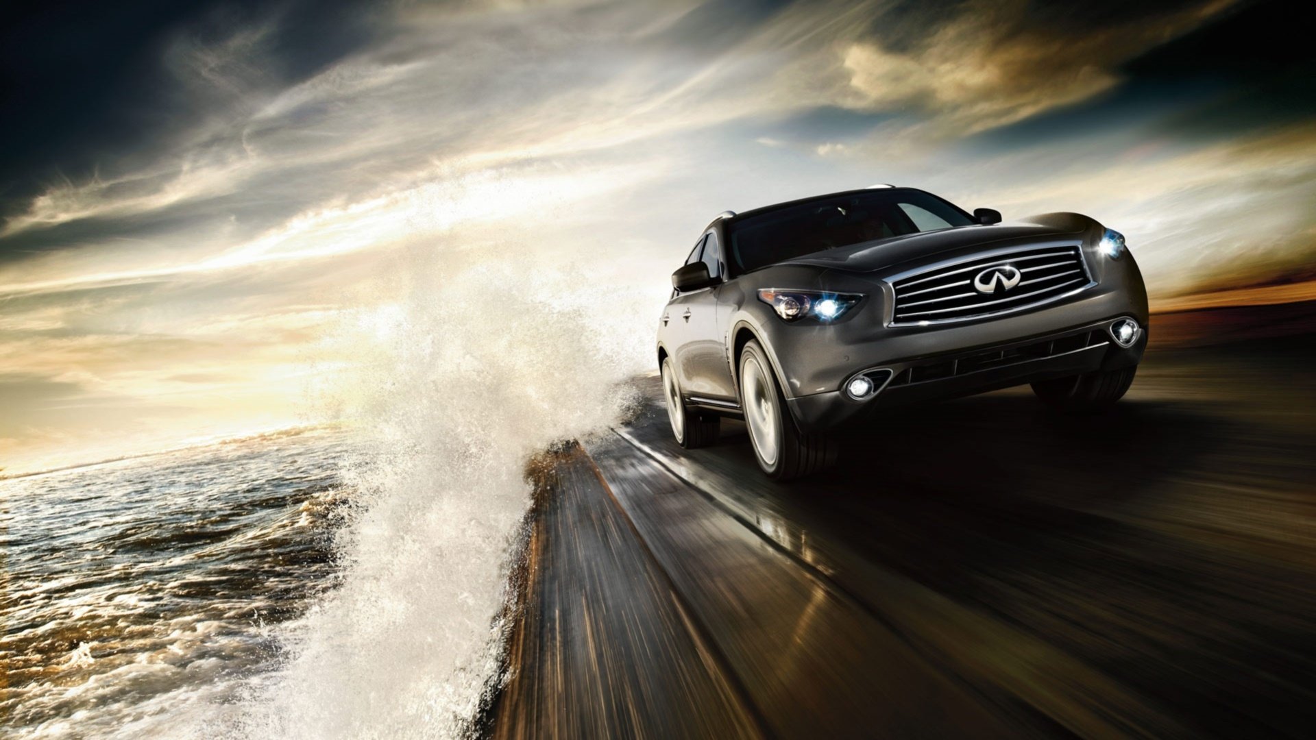 HD desktop wallpaper featuring an Infiniti QX70 speeding along a wet coastal road with dramatic clouds and ocean waves in the background.