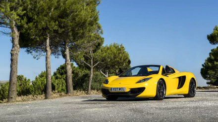 Yellow McLaren MP4-12C Spider on a sunlit roadside with pine trees, HD PC desktop wallpaper and background.