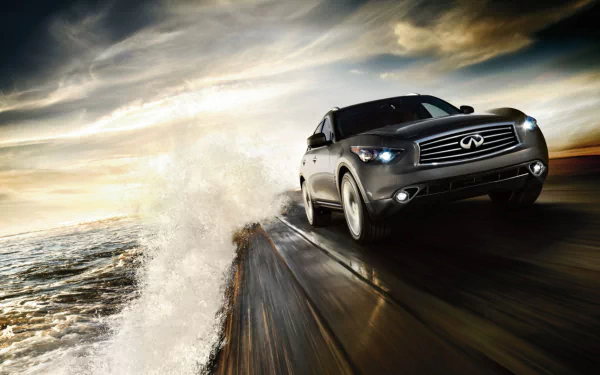 HD desktop wallpaper featuring an Infiniti QX70 speeding along a wet coastal road with dramatic clouds and ocean waves in the background.