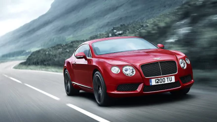 A red Bentley Continental GT V8 cruising on a coastal road, captured in a high-definition image for a desktop wallpaper background.