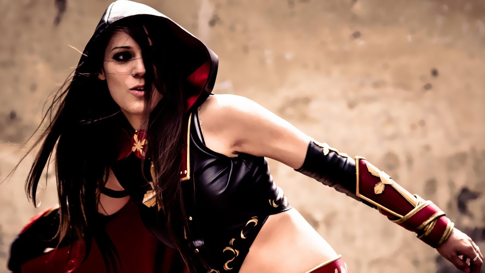 A woman in striking cosplay, wearing a dark hood and stylish outfit, poses dramatically against a textured background, creating a dynamic and captivating HD desktop wallpaper.