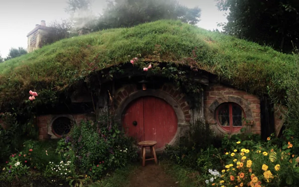 HD desktop wallpaper from The Hobbit: An Unexpected Journey featuring a charming hobbit hole surrounded by vibrant flowers and lush greenery.