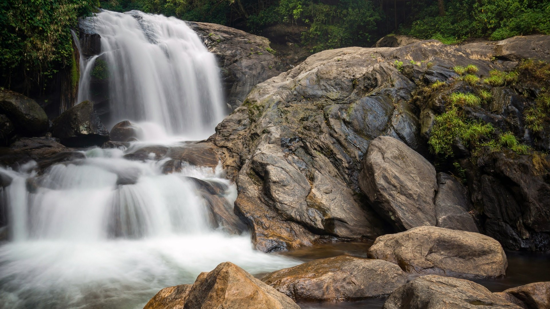 A 4K Ultra HD PC desktop wallpaper featuring a serene nature scene with a cascading waterfall flowing over rocks surrounded by lush greenery.