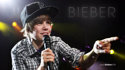 Young male artist performing live with a microphone, wearing a baseball cap and plaid shirt, with stage lights in the background, as HD desktop wallpaper.