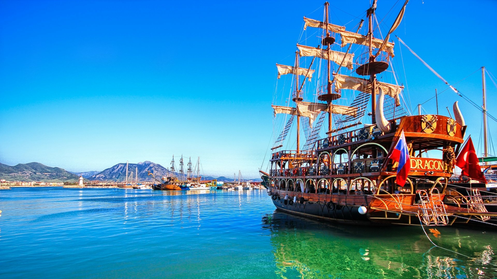 HD desktop wallpaper featuring a vibrant scene with the Dragon ship and other tall ships in a crystal-clear blue harbor under a bright sky.