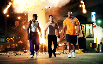 Three muscular men walk confidently through a chaotic scene of explosions, featuring characters Adrian Doorbal, Daniel Lugo, and Paul Doyle from the movie Pain & Gain, starring Dwayne Johnson and Mark Wahlberg.