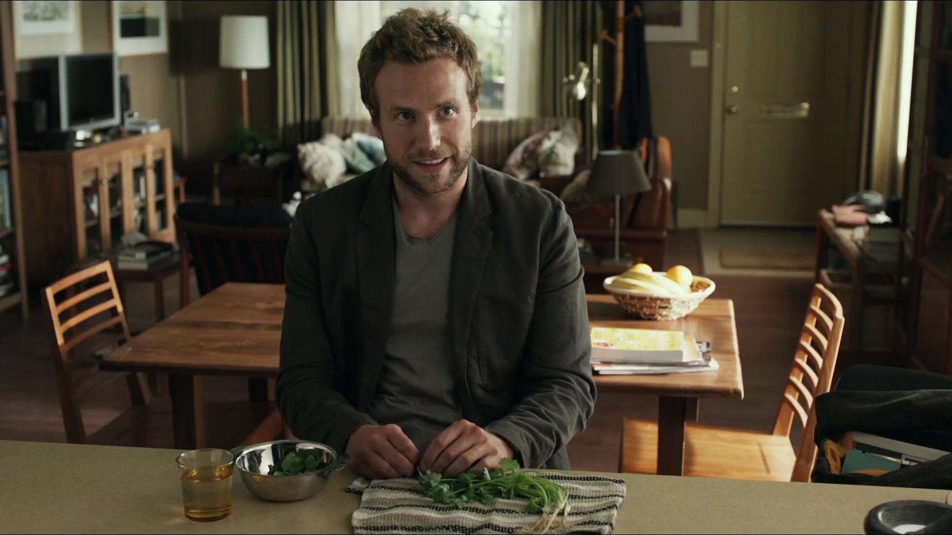 HD PC desktop wallpaper (movie: Life of Pi) — a man chops herbs at a kitchen table, warm light and a cozy, lived-in living room visible behind him.