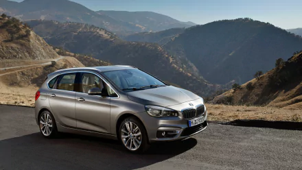 Silver BMW 2 Series Active Tourer parked on a mountain road with winding peaks in the background — HD PC desktop wallpaper showcasing the compact MPV and scenic alpine landscape.